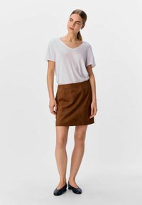 Gonna in suede marrone con taglio dritto e cuciture laterali, abbinata a una t-shirt rosa chiaro con scollo a V. Le scarpe nere flat completano l'outfit.