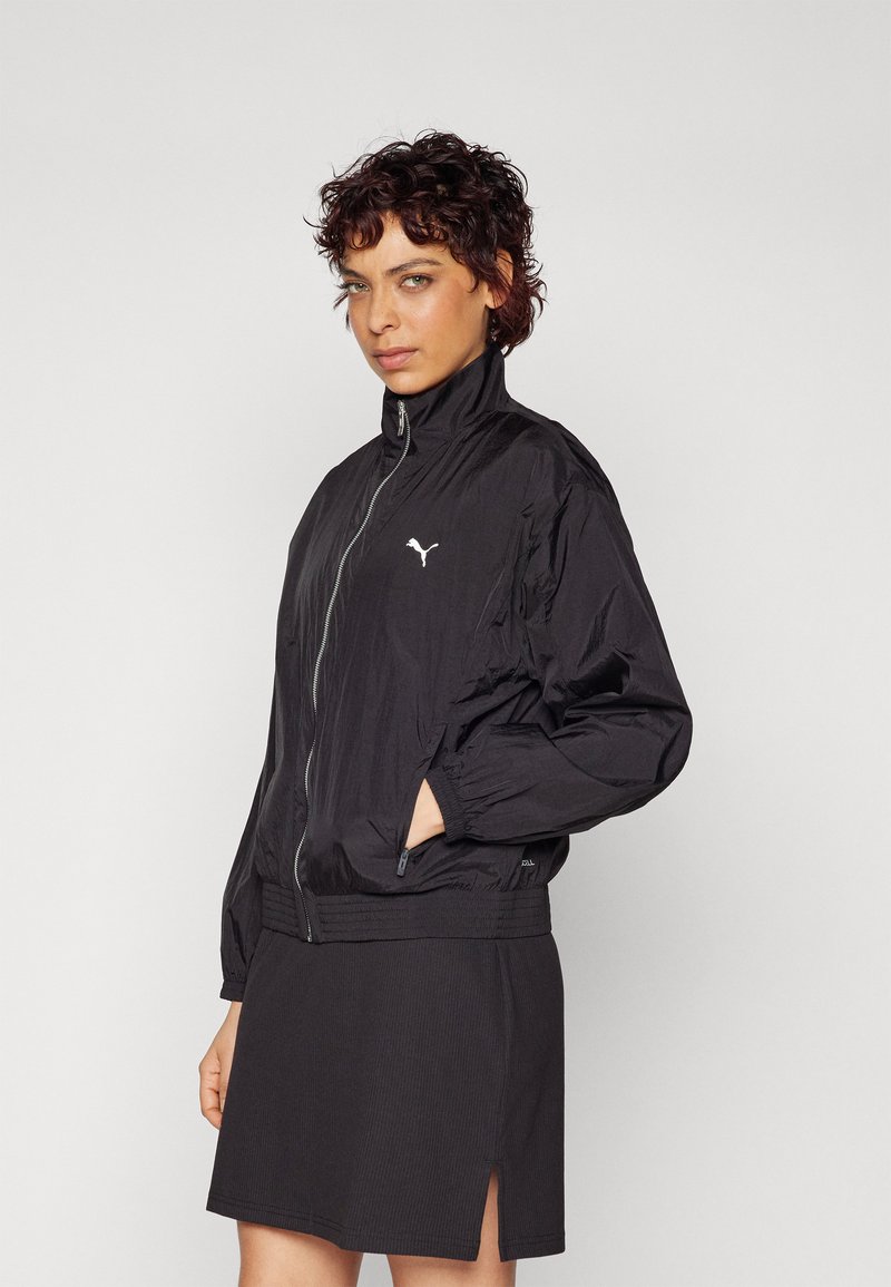 Veste bomber en nylon noir avec un col montant et une fermeture éclair. Elle dispose de poignets élastiques et d'un petit logo blanc sur la poitrine gauche.