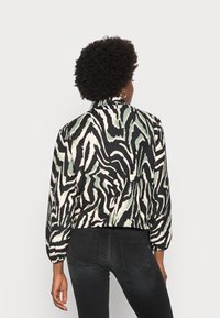 Casaco curto em preto com padrão zebrado abstrato em creme e verde. Apresenta colarinho, mangas longas e punhos elásticos.