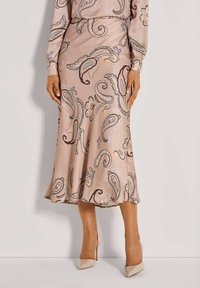 Helles rosa Kleid mit paisleymuster in Dunkelbraun, Blau und Orange. Ausgestellter Saum und glatte Textur, kombiniert mit beigen High Heels.