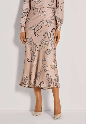 Helles rosa Kleid mit paisleymuster in Dunkelbraun, Blau und Orange. Ausgestellter Saum und glatte Textur, kombiniert mit beigen High Heels.