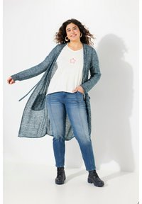 Pitkä, avointa etuosaa oleva kardigan, jossa on teksturoitua turkoosia neulosta, yhdistettynä valkoiseen T-paitaan, jossa on pastellivärinen tähden kuvio, sekä vaaleansinisiin farkkuihin. Mustat nilkkasaappaat.