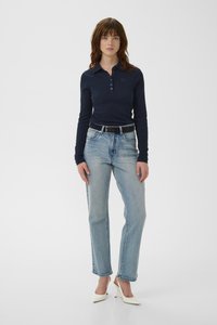 Polo de manga larga azul marino con botonadura, combinado con vaqueros de pierna recta en azul claro y tacones blancos de punta afilada. Diseño sencillo.