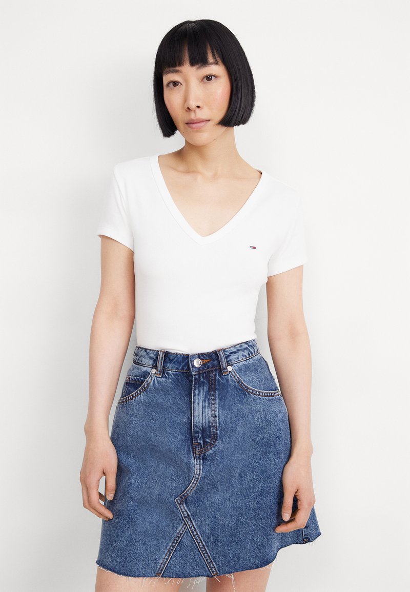 Hvit V-hals skjorte med korte ermer kombinert med en blå denim A-linje skjørt med frynset kant og synlige sidelommer.