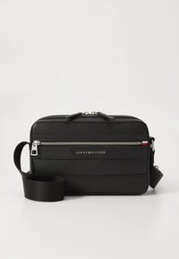 Black textured leather crossbody bag with silver zipper, adjustable strap, and small Tommy Hilfiger logo with red, white, and blue flag detail.