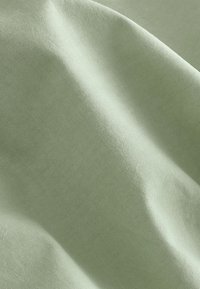 Tissu en coton vert clair avec une texture lisse, présentant des plis subtils et un motif de tissage régulier. Idéal pour les vêtements ou la tapisserie.