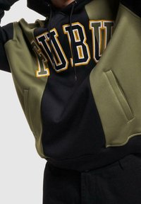 Huvtröja med oversized passform, med svarta och olivgröna paneler, tydliga vita och gula märkesbokstäver samt sidofickor.