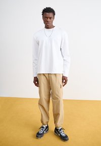 Hvid langærmet skjorte, beige cargo bukser og sorte sportsko med hvide accenter. Afslappet pasform med et enkelt, rent design.