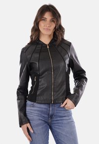 Giacca in vera pelle nera con zip frontale, design aderente e tasche laterali. Presenta cuciture verticali e uno stile sportivo con cappuccio.