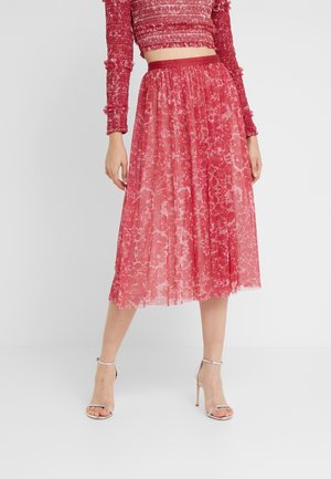 Różowa plisowana spódnica z przezroczystej koronkowej tkaniny z kwiatowymi wzorami, zestawiona z dopasowanym teksturowanym crop topem. Srebrne sandały na obcasie.