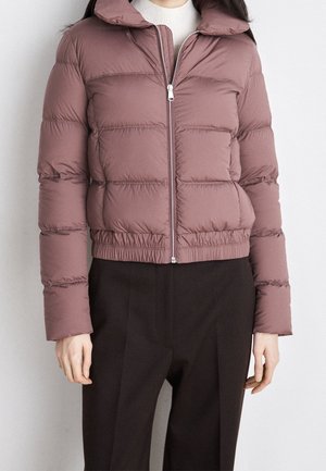 Personne portant une doudoune mauve avec fermeture éclair à l'avant et un ourlet élastique, associée à un pantalon noir et un pull à col roulé blanc.