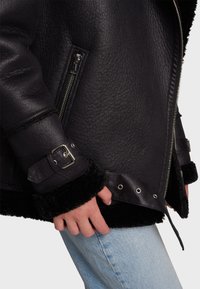 Black leather jacket featuring a textured finish, zippered pockets, and plush black fur accents at the cuffs and hem.