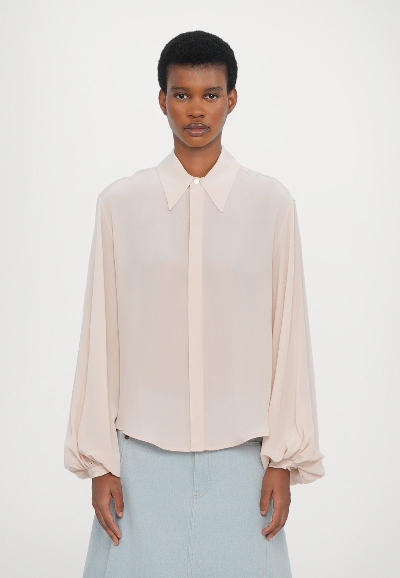 Blusa de manga larga en rosa claro con cuello puntiagudo y cierre de botones; cuenta con mangas abullonadas y un tejido suave y ligero.