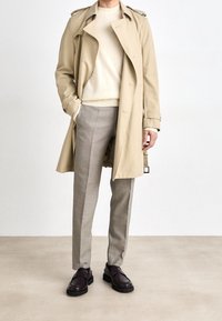Beige trenčkot, krémový svetr, světle šedé vzorované kalhoty, tmavě hnědé slip-on boty s tlustou podrážkou. Formální příležitostný outfit.