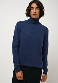 Pull en col roulé bleu marine en tissu doux et texturé. Présente des poignets et un ourlet côtelés, avec une coupe décontractée et des manches longues.