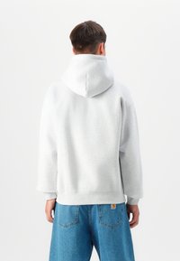 Moletom cinza claro com um capuz grande e macio, costuras de ombro caídas e um corte relaxado, combinado com jeans azul. Design minimalista.