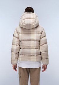 Vadderad jacka i beige rutigt tyg med huva. Har en boxig form, horisontellt kviltade sektioner och elastiska muddar.