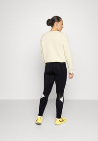 Sweatshirt crema, leggings neri con dettagli in rete e accenti grigi, e scarpe da ginnastica gialle. Design semplice e aderente. Vista posteriore.