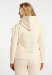 Crème hoodie met een zachte textuur, kangaroozak en trekkoordkap, met contrasterende stiksel langs de manchetten en de zoom.