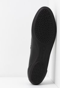 Semelle de chaussure noire avec des motifs de semelles circulaires, affichant un design flexible et le nom de la marque "Geox" au centre.