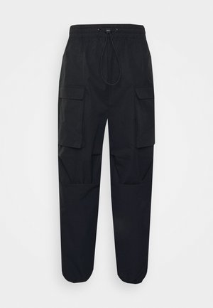 Pantalon cargo noir avec taille élastique et poignets aux chevilles, équipé de deux grandes poches à rabat sur les cuisses et d'une fermeture à cordon.