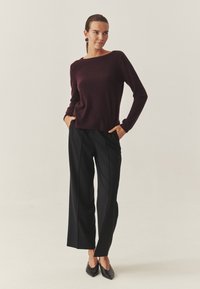 Burgundijas adīta džemperis ar plašu kakla izgriezumu, kombinēts ar melniem pielāgotiem biksēm ar taisnu griezumu un krokām, pabeigts ar melniem papēžiem.