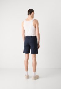 Calções de algodão azul-marinho com cintura elástica, bolsos traseiros e um corte ajustado, combinados com uma t-shirt branca e sapatos bege.