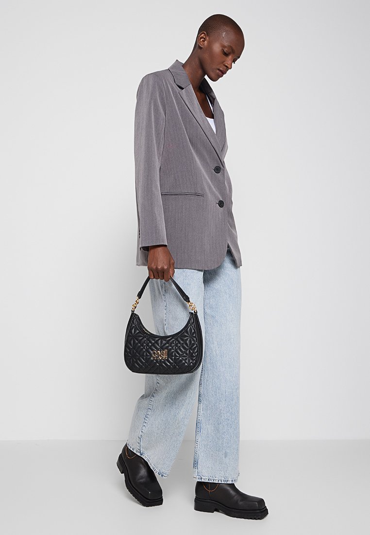 Grauer Nadelstreifen-Blazer mit schwarzen Knöpfen, hellblaue Schlagjeans und eine strukturierte schwarze Handtasche mit goldenem Logodetail.