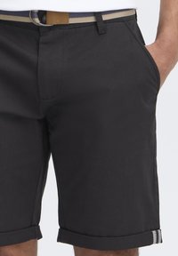 Shorts noirs en tissu léger, avec des ourlets retroussés à motif rayé, et une ceinture beige avec une boucle simple.