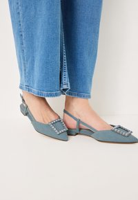 Scarpe slingback con punta affusolata in tessuto blu chiaro testurizzato, dotate di una fibbia quadrata adornata di strass e tacco basso impilato.