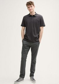 Szara polo z paskami i krótkimi rękawami, połączona z szarymi spodniami teksturowanymi oraz jasnoszarymi trampkami. Warto zwrócić uwagę na detal kieszonki na koszulce.