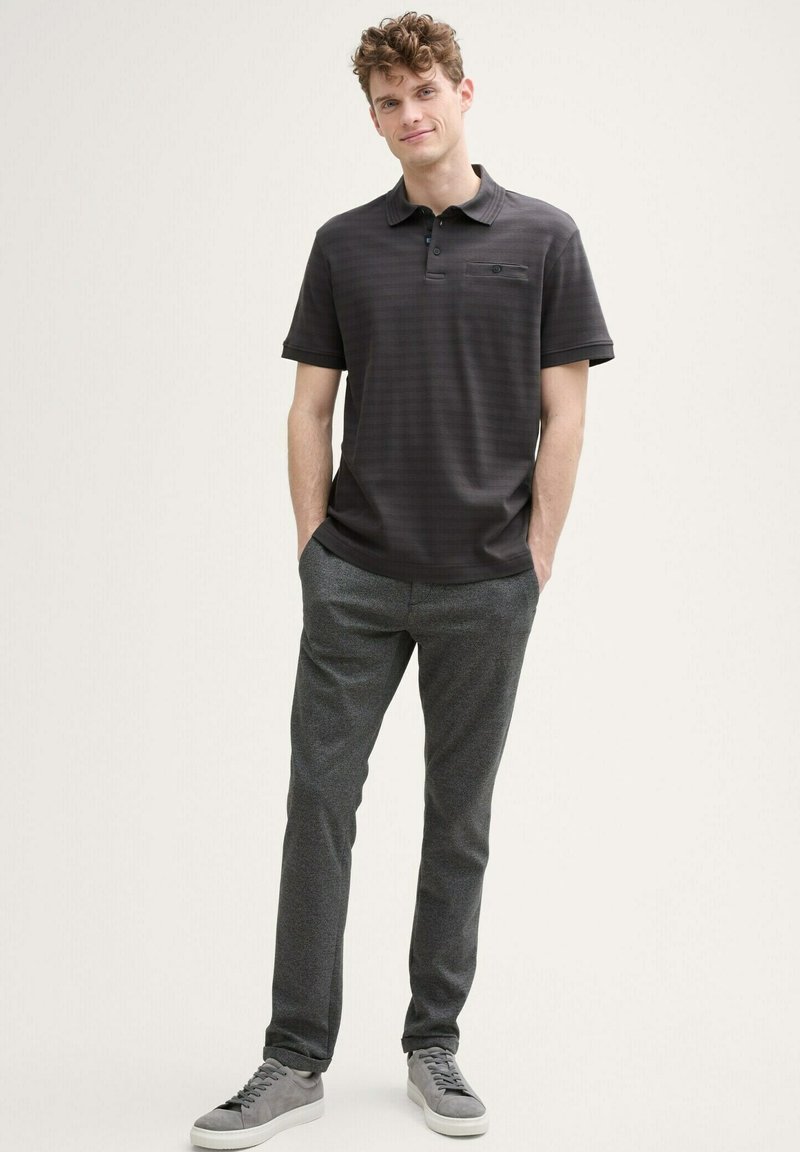 Szara polo z paskami i krótkimi rękawami, połączona z szarymi spodniami teksturowanymi oraz jasnoszarymi trampkami. Warto zwrócić uwagę na detal kieszonki na koszulce.