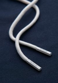 Białe plecione końcówki sznurówek z metalowymi agletami wygrawerowanymi słowem "ombre" na granatowym tle.