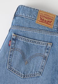 Poche arrière d'un jean Levi's bleu clair avec couture signature, étiquette rouge Levi's et étiquette en cuir marron Levi Strauss & Co. sur la ceinture.