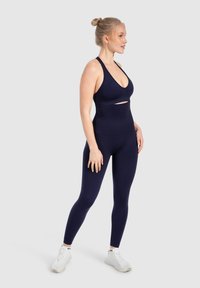 Conjunto deportivo azul marino que incluye un sujetador deportivo ajustado con detalles recortados y leggings de cintura alta, confeccionado con una tela elástica y suave.