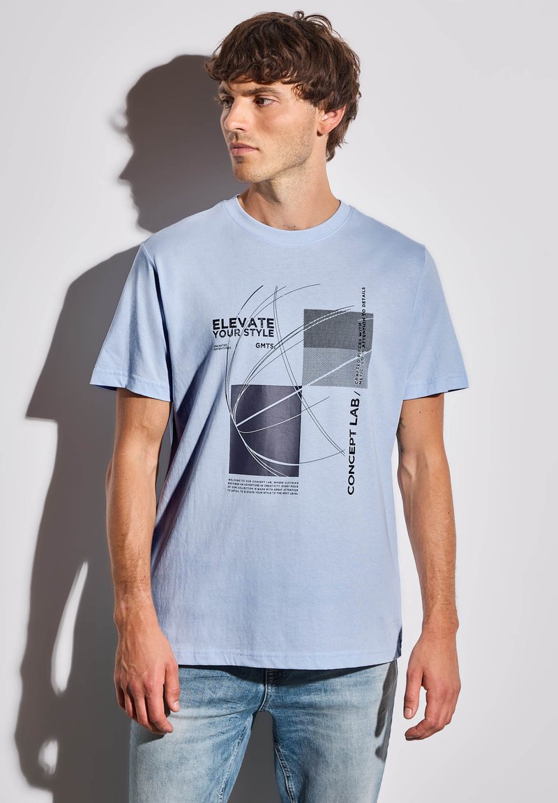 T-shirt en coton bleu clair avec impression graphique noire présentant diverses formes et du texte. Manches courtes, col rond, coupe décontractée.