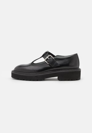 Zapato Mary Jane de cuero negro con suela gruesa de tacos y hebilla plateada en la correa lateral, mostrado en perfil lateral sobre fondo blanco.