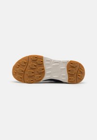 Sålen av en sneakers som har en kombinasjon av gummigummi og hvit gummi, med markerte grep mønstre og en mørkfarget overdel.