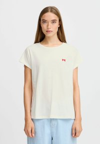 Kortærmet, lys beige t-shirt lavet af bomuld med rund hals og et lille rødt sløjfe-logo på venstre bryst. Glat tekstur.