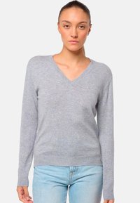 Hellgrauer V-Ausschnitt-Pullover aus weichem Material, mit langen Ärmeln und geripptem Saum. Kombiniert mit hellblauen Jeans.