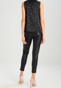 Blouse noire sans manches à motif d'étoiles blanches, associée à un pantalon en cuir noir ajusté et des talons hauts de couleur claire. Textures lisses partout.