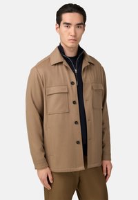 Ljusbrun ullblandad jacka med krage, två framfickor och knappar. Bärs över en marinblå tröja.