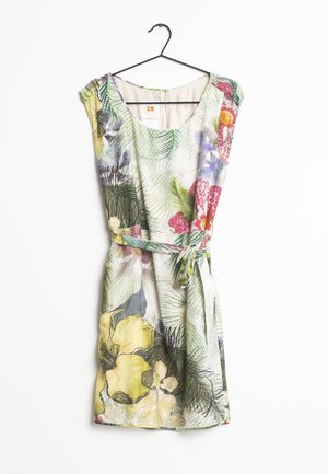 Robe sans manches longueur genoux avec encolure ronde, imprimé floral tropical en vert, jaune, rouge et violet, ceinture nouée à la taille, suspendue sur un cintre noir.