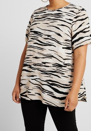 Lockere kurzärmelige Bluse mit beigefarbenen, schwarzen und weißen Zebra-Streifen, getragen mit schwarzen Hosen von einer Person.