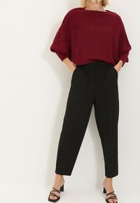 Pull en tricot bordeaux à coupe ample, motif texturé à l'avant, associé à un pantalon noir fuselé taille haute et des talons noirs à lanières.