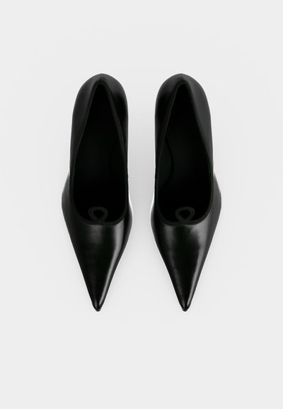 Paire de chaussures noires à talons aiguilles et bouts pointus vues de dessus sur un fond blanc uni.