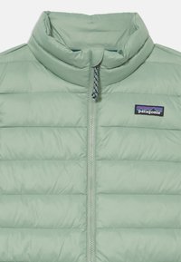 Colete acolchoado verde claro com gola alta, design de quiltado horizontal, fecho de correr completo e um pequeno logotipo da Patagonia no lado esquerdo do peito.