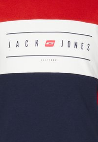 Camiseta de color bloque rojo, blanco y marino hecha de algodón, con un logo rectangular que presenta el texto "JACK JONES" y el detalle "JJ//1990".