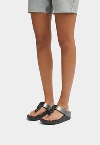 Zwarte flip-flops met een zachte band met decoratieve accenten, geplaatst op een gestructureerde donkere zool. Het ontwerp is minimalistisch en modern.
