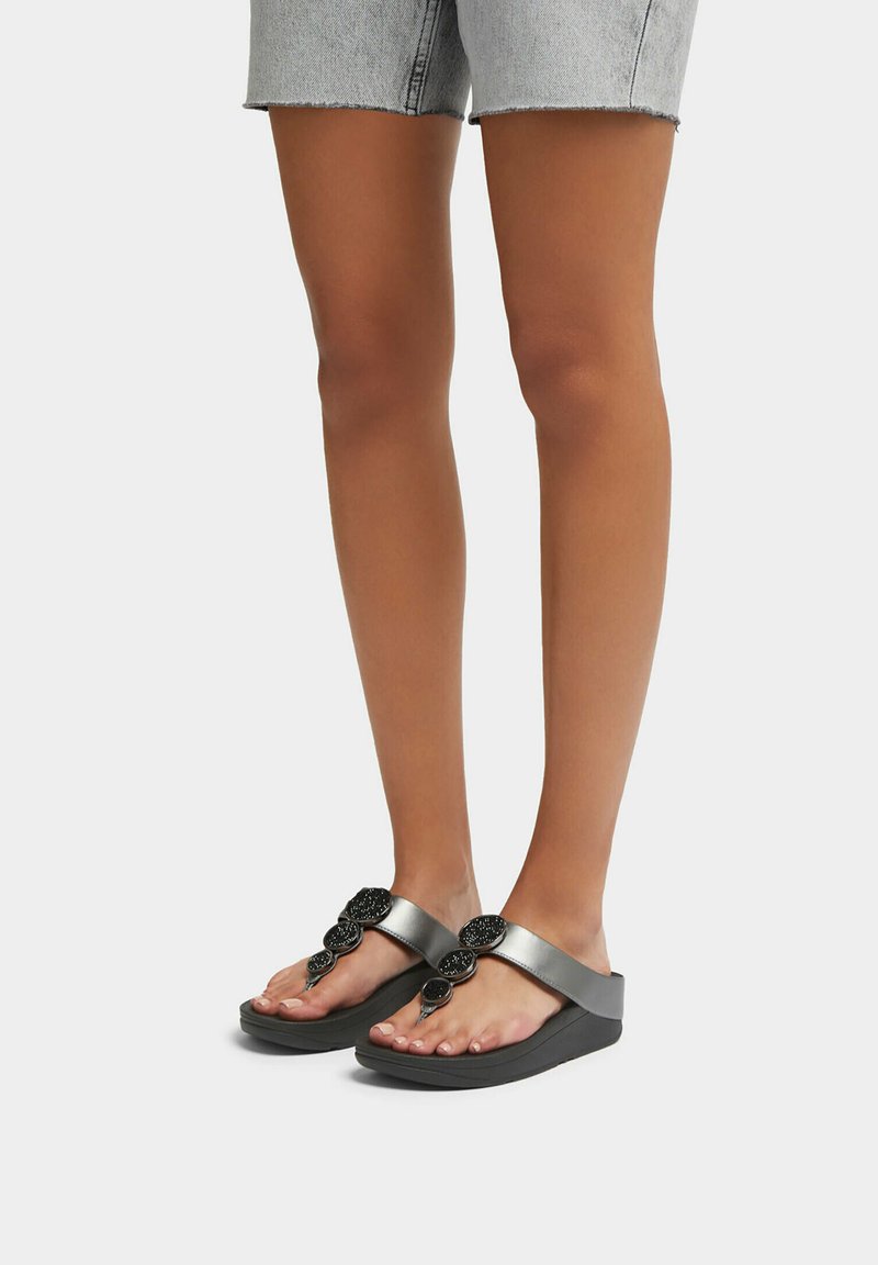 Zwarte flip-flops met een zachte band met decoratieve accenten, geplaatst op een gestructureerde donkere zool. Het ontwerp is minimalistisch en modern.